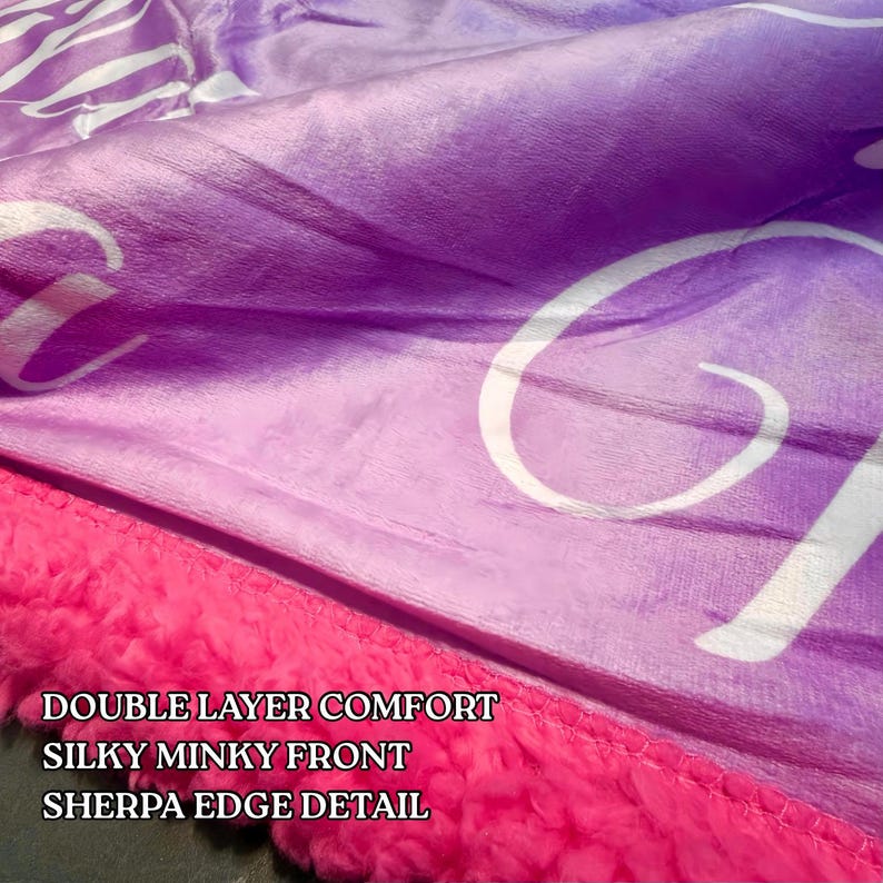 Puede incluir: Primer plano de una manta de felpa en tonos morados y rosas. La manta presenta un frente de vis&oacute;n sedoso y un borde de sherpa rosa brillante. El texto blanco en la manta dice "DOUBLE LAYER COMFORT, SILKY MINKY FRONT, SHERPA EDGE DETAIL."