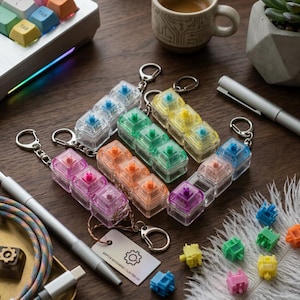 Könnte beinhalten: Eine Sammlung farbenfroher mechanischer Tastaturschalter-Schlüsselanhänger in verschiedenen Farben, darunter Blau, Grün, Gelb, Rosa und Orange. Jeder Schlüsselanhänger hat drei Schalter in einem transparenten Kunststoffgehäuse mit einem Metall-Schlüsselring. Einzelne Schalter sind ebenfalls abgebildet.
