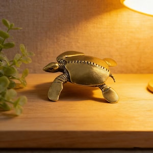 May include: A brass turtle figurine with detailed features, including a segmented shell and flipper-like legs. The turtle is positioned on a wooden surface, with a warm light illuminating the scene. The figurine is a decorative item.