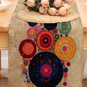 Puede incluir: Un camino de mesa decorativo con un fondo beige y diseños de círculos concéntricos coloridos en tonos de rojo, naranja, amarillo, azul y verde. Un salvamanteles de paja tejida y rosas rosas adornan la parte superior, agregando elegancia a la mesa.