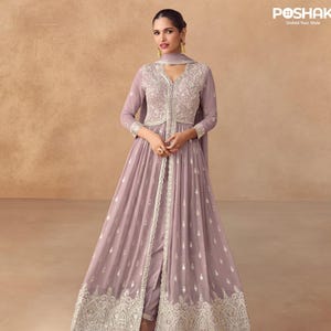 Puede incluir: Un vestido de noche malva con intrincados bordados plateados. El vestido presenta una falda larga y fluida, un corpiño ajustado y una bufanda a juego. El diseño incluye una abertura frontal y adornos detallados, creando un look elegante. La marca "POSHAK" es visible.