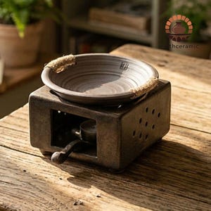 Puede incluir: Un juego de tres tazas de cerámica con un esmalte moteado de color crema. Cada taza presenta un diseño pintado a mano diferente: una hoja azul y verde, una flor amarilla y una baya roja. Las tazas tienen una forma simple y redondeada.