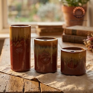 Può includere: Tre vasi in ceramica di diverse altezze, con una sfumatura di colori dal marrone al rosso-marrone. I vasi hanno una finitura lucida e un design unico e strutturato. Il logo earthceramic è visibile sullo sfondo.