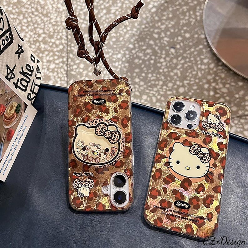May include: Two phone cases with a leopard print design and Hello Kitty graphics. One case has a pop-up grip with Hello Kitty characters. The cases are brown and gold with the word "Lucky" printed on them.