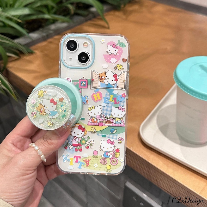 Pu&ograve; includere: Custodia trasparente per telefono con design Hello Kitty, con un supporto per telefono. La custodia ha un bordo azzurro ed &egrave; decorata con personaggi di Hello Kitty, fiori e la scritta "HELLO". Il supporto per telefono &egrave; verde chiaro e presenta un design Hello Kitty.