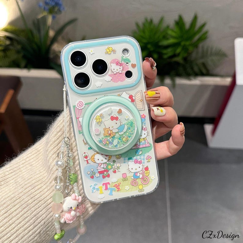 Pu&ograve; includere: Custodia trasparente per telefono con design Hello Kitty, bordo azzurro e supporto abbinato. La custodia presenta un design glitterato e animato con personaggi e accessori di Hello Kitty. &Egrave; attaccato un ciondolo di perline con una figura di Hello Kitty.