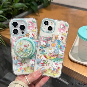 Pu&ograve; includere: Custodie trasparenti per telefono con un design di Hello Kitty. Le custodie hanno un bordo azzurro e un supporto per telefono con glitter. Il design include personaggi di Hello Kitty, fiori e altri elementi decorativi. Le custodie sono per un telefono.