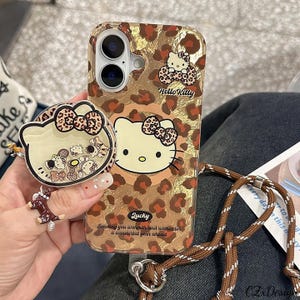 May include: A clear phone case with a leopard print design and Hello Kitty graphics. The case has a matching pop socket and a brown and white lanyard. The text on the case says "Lucky" and "Sending you warmth and wishes for a wonderful year ahead."
