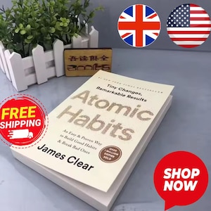 May include: A hardcover book titled "Atomic Habits" by James Clear. The book has a cream-colored cover with the title in large, glittery letters. The cover also includes the text "Tiny Changes, Remarkable Results" and "An Easy & Proven Way to Build Good Habits & Break Bad Ones."