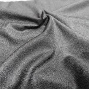 Könnte beinhalten: Nahaufnahme eines dunkelgrauen Stoffes mit leichtem Glanz. Das Material ist fein gewebt und zeigt Textur und Falten, die Schatten erzeugen. Der Stoff wirkt weich und fällt natürlich, was darauf hindeutet, dass er für Kleidung oder Heimdekoration geeignet ist.