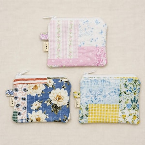 May include: Three rectangular zipped pouches made of quilted fabric. The top pouch features pink stripes and floral patterns. The bottom left pouch has blue and white floral designs. The bottom right pouch displays blue and yellow patterns.