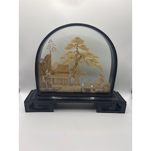 May include: A decorative diorama featuring a miniature landscape scene. The scene includes a detailed building, trees, and figures, all encased within a glass dome and set on a black base. The diorama is approximately 12 inches wide.