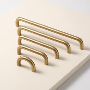May include: A set of five brass cabinet pulls arranged in a cascading size order from longest to shortest. Each pull features a smooth, rounded U-shaped design with a matte metallic finish, consisting of two vertical mounting posts and a horizontal bar.