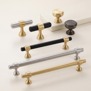 May include: A collection of cabinet hardware including various drawer pulls and knobs in brushed gold, matte black, and silver finishes. The hardware features cylindrical bars and round bases, showcasing a mix of long and short handle designs.