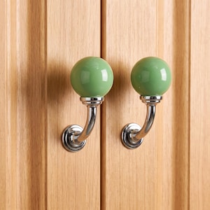 Peut inclure: Deux boutons de porte sphériques en céramique vert sauge montés sur des bases métalliques chromées polies et incurvées. Chaque bouton présente une finition lisse et brillante, fixée sur une plaque circulaire chromée.