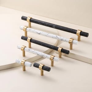 May include: A collection of six cabinet pulls in varying lengths, featuring cylindrical bars with black or white marble patterns and brushed gold metal posts. The hardware includes both single-knob styles and longer handles with two mounting points.