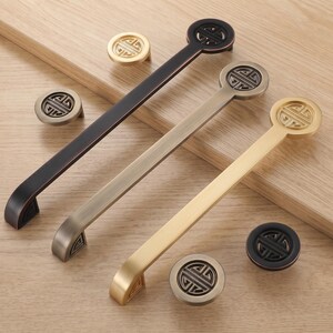 May include: Three long cabinet pulls and four round knobs in black, antique brass, and brushed gold finishes. Each piece features a circular head with an intricate openwork geometric pattern. The hardware is arranged in a diagonal composition.