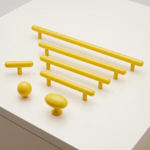 May include: A collection of bright yellow cabinet hardware including four linear bar pulls of varying lengths, one T-shaped handle, one spherical knob, and one oval-shaped knob, all featuring a smooth, solid-colored matte finish.