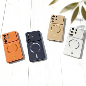 May include: Four mobile phone cases in orange, navy, gold, and white, each with a textured finish. The cases have a camera section at the top and a circular design with a small symbol at the bottom. The cases are on a white wooden surface.