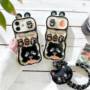 May include: Two white phone cases with black cat designs and the text "Cool cats". Each case has a 3D cat figure and a black strap. One case has a small orange fruit design.