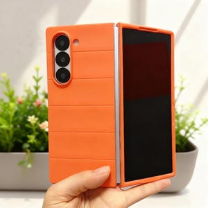 Puede incluir: Funda de teléfono naranja brillante con una cámara de tres lentes y una pantalla negra. La funda tiene un diseño texturizado con líneas horizontales. El teléfono está parcialmente abierto.