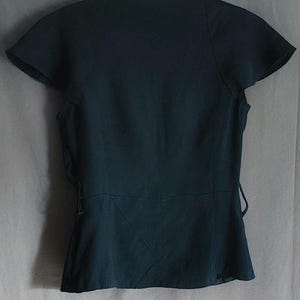 May include: Dark teal-colored top with short, flared sleeves and a V-neckline. The back of the top features a fitted waist with a subtle peplum and tie details on the sides. The top is hanging on a white hanger.