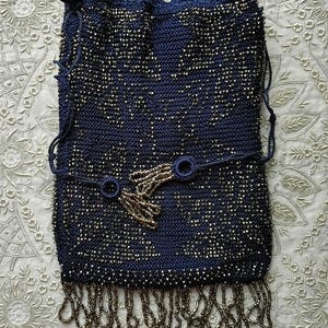 May include: A navy blue beaded handbag with a drawstring closure. The bag features a decorative beaded design and a beaded fringe along the bottom. The bag has a strap with two circular accents and a beaded tassel.