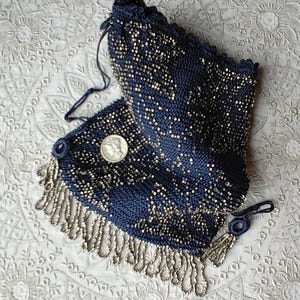 May include: A vintage navy blue beaded purse with silver-toned accents and fringe. The purse features a drawstring closure and a small coin. The intricate beadwork creates a textured surface, showcasing a classic design.