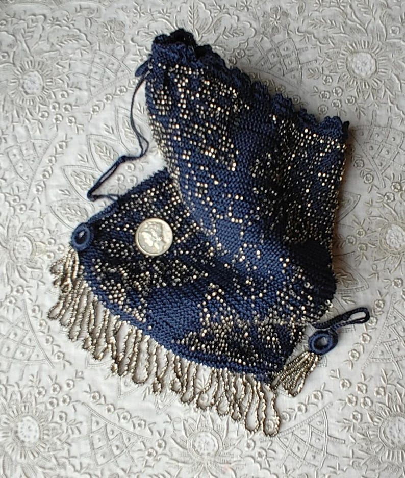 May include: A vintage navy blue beaded purse with silver-toned accents and fringe. The purse features a drawstring closure and a small coin. The intricate beadwork creates a textured surface, showcasing a classic design.