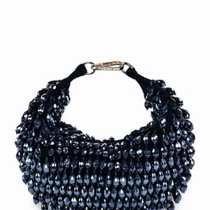 Può includere: Una borsetta blu scuro con perline, con un cinturino in velluto nero e una chiusura color oro. La borsa è densamente ricoperta di piccole perline a forma di goccia, creando un effetto strutturato e scintillante. Il design è elegante e adatto alla sera.