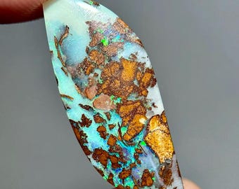 May include: A polished marquise-shaped boulder opal gemstone featuring a vibrant play of color with bright cyan and green flashes set against a natural dark brown ironstone matrix. The stone has a smooth, glossy surface and irregular patterns.