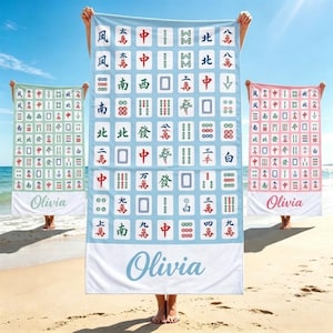 May include: Three rectangular beach towels featuring a grid of mahjong tile graphics. The center towel is light blue, the left is light green, and the right is light pink. Each towel displays the name Olivia in a cursive script at the bottom.