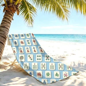 May include: A beach chair featuring a light blue fabric cover printed with a repeating pattern of various Mahjong tiles. The tiles display traditional Chinese characters, numbers, and circular symbols in red, green, and black ink colours.
