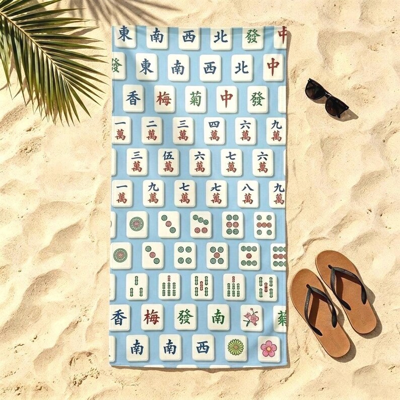 May include: A rectangular beach towel featuring a light blue background with a repeating pattern of white Mahjong tiles. The tiles display various traditional Chinese characters, numbers, and floral symbols in red, green, and black ink colors.