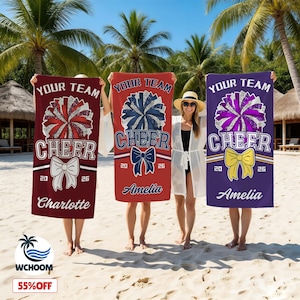 May include: Three rectangular beach towels featuring the text YOUR TEAM CHEER, a glittery pom-pom graphic, a bow, the year 2026, and a personalized name. The towels are maroon with Charlotte, red with Amelia, and purple with Amelia printed on them.
