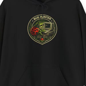 Può includere: Felpa con cappuccio nera con grafica frontale. La grafica presenta una creatura verde con un computer e una coccinella, con le parole "BUG HUNTER" e codice binario. La felpa ha una tasca frontale e un cappuccio con coulisse.