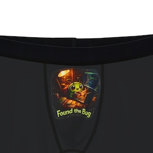 Puede incluir: Bóxers negros con un gráfico colorido que presenta un personaje de dibujos animados y el texto "Found the Bug" en verde. La ropa interior tiene una cintura negra y un ajuste cómodo.