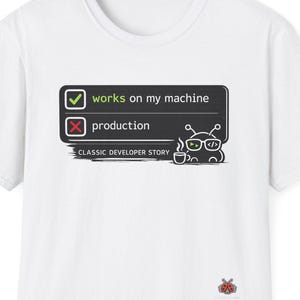 以下が含まれることがあります： 「works on my machine」と「production」の文字が描かれたグラフィックが特徴の白いTシャツ。グラフィックにはメガネをかけた漫画のキャラクターとコーヒーカップが含まれています。「CLASSIC DEVELOPER STORY」の文字もプリントされています。