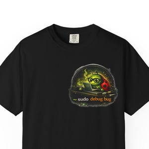 May include: Black t-shirt with a cartoon bug wearing glasses and working on a laptop. The design includes the text "~ sudo debug bug" in orange. The bug is green with red accents, set against a dark background.