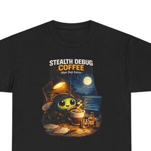 以下が含まれることがあります： 黒いTシャツ。大きな目をした漫画のハチのキャラクターが、コンピューターのある机でコーヒーを飲んでいます。「STEALTH DEBUG COFFEE - Night Shift Edition」の文字が画像の上に印刷されています。
