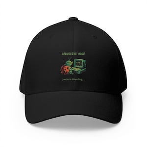 Può includere: Cappellino da baseball nero con visiera curva. Il cappellino presenta una grafica di una coccinella al computer con il testo "DEBUGGING MODE" e "just one more bug..." in verde e bianco.