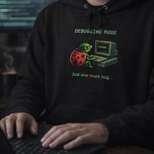 May include: Black hoodie with a graphic of a ladybug working on a computer, with the text "DEBUGGING MODE" and "Just one more bug...". The ladybug has a red shell with black spots. The computer screen displays "CODE".