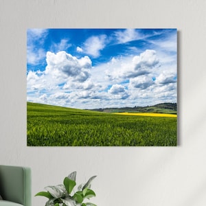 Könnte beinhalten: Leinwanddruck einer malerischen Landschaft. Ein leuchtend blauer Himmel mit weißen Wolken über einem hügeligen grünen Feld. Ein Streifen gelber Blumen setzt einen Farbtupfer in der Ferne.