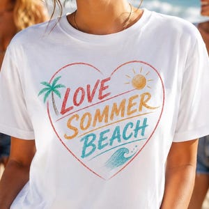 Könnte beinhalten: Ein weißes T-Shirt mit kurzen Ärmeln und einem großen roten Herzumriss auf der Brust. Im Inneren des Herzens steht der Text LOVE SOMMER BEACH in bunten Buchstaben, ergänzt durch eine grüne Palme, eine gelbe Sonne und eine blaue Meereswelle.