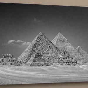 Könnte beinhalten: Schwarz-Weiß-Leinwanddruck der Pyramiden von Gizeh in Ägypten. Das Bild zeigt die Pyramiden in der Wüstenlandschaft unter einem klaren Himmel mit ein paar Wolken. Die Pyramiden sind das Hauptmerkmal.
