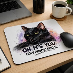 Può includere: Tappetino per mouse rettangolare bianco con un gatto nero con occhi gialli e la scritta "OH, IT'S YOU HOW PREDICTABLE." Il gatto è ambientato su uno sfondo in stile acquerello con schizzi viola e rosa. Un mouse per computer nero è accanto.