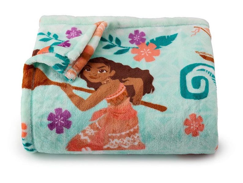 May include: A folded turquoise blanket featuring a cartoon illustration of a woman holding a wooden oar. The blanket has floral and leaf patterns in pink, purple, and teal. The blanket is made of a soft, plush material.