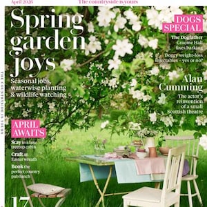 Op de afbeelding: De cover van Country Living magazine, april 2026, met de kop "Spring garden joys". Artikelen over seizoensgebonden werk, beplanting en wilde dieren. Een tuintafel is gedekt met witte stoelen en een bloemenachtergrond.