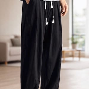 May include: Black drawstring pants with a relaxed fit. The pants have a white drawstring and are paired with a black and white striped shirt. The pants are made of a lightweight material.