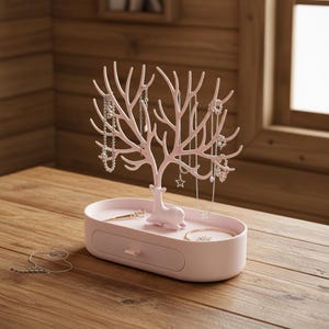 May include: A pink jewelry organizer with a tree-like design for hanging necklaces and bracelets. The base has a drawer and a small deer figurine. The organizer is on a wooden surface, with jewelry displayed on the branches.